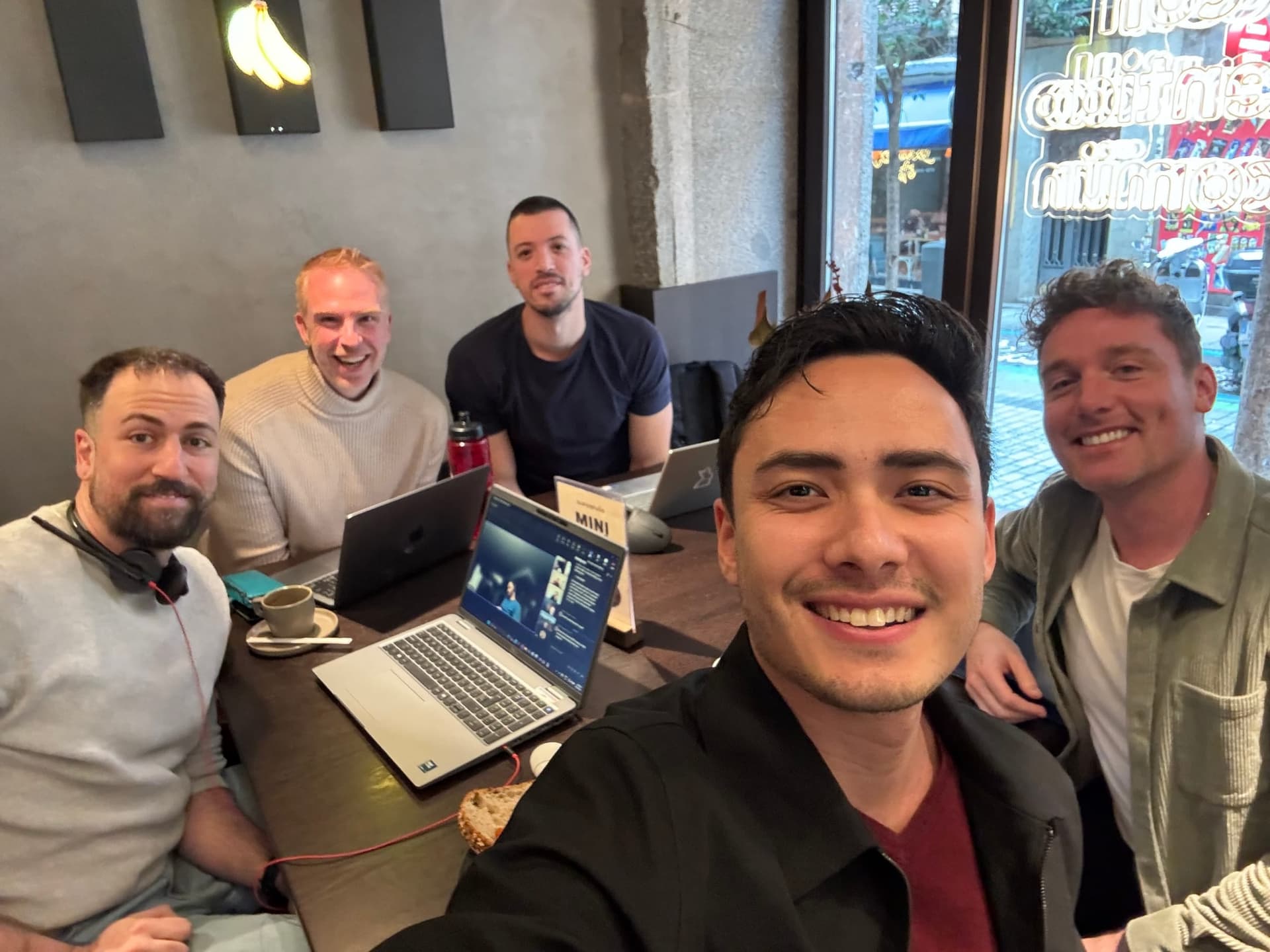 A group selfie at the coworking table with laptops and snacks.