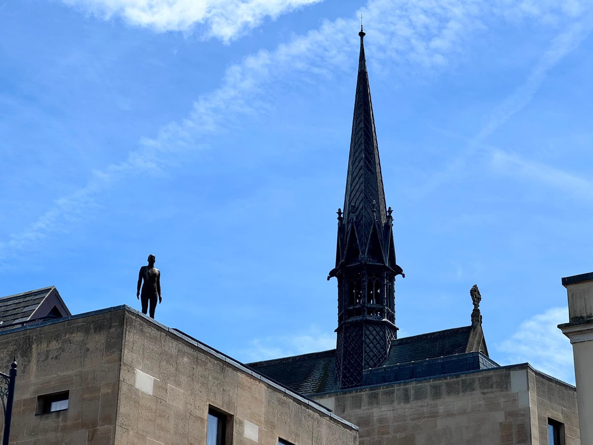 A silhouetted figure stands on a rooftop against a spire and blue sky.