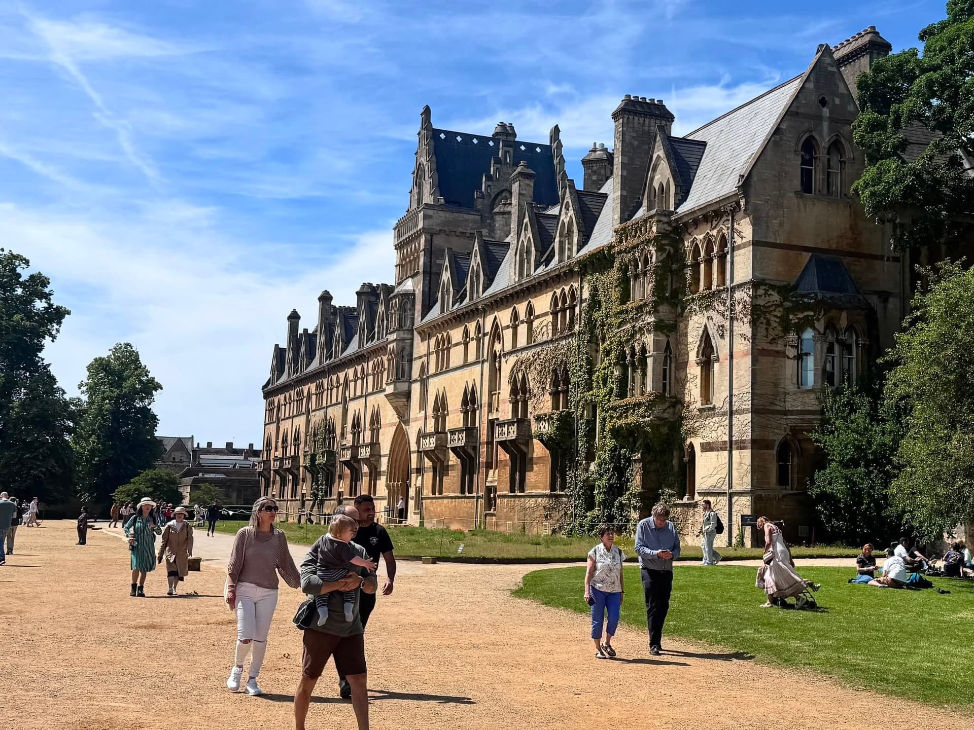Visitors cross the lawn before an Oxford college's grand facade.